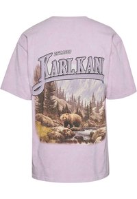 Lavender cotton t-shirt featuring a graphic of a bear in a forest scene, with "KARL KANI" and "EST.1989" printed above the artwork.