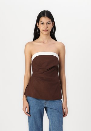 Haut sans bretelles marron avec une bande blanche, présentant un design ajusté et un léger drapé. Associé avec un jean large bleu clair.