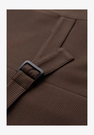 Brązowa teksturowana tkanina z tkanym wzorem, z czarną prostokątną klamrą zabezpieczającą pasek. Materiał wydaje się trwały i solidny.