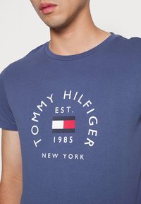Námořnická modrá bavlněná tričko s kulatým výstřihem a grafickým potiskem s textem "TOMMY HILFIGER EST. 1985 NEW YORK" a logem vlajky.
