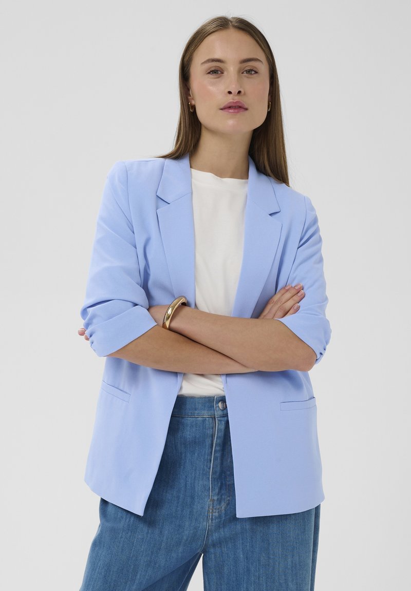 Lichtblauwe blazer met een getailleerd ontwerp, revers met inkeping, opgerolde mouwen en een enkele voorzak, gecombineerd met een wit t-shirt en spijkerbroek.