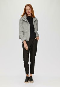 Graue, taillierte Jacke mit Reißverschluss und Druckknopfverschluss, ausgestattet mit zwei Fronttaschen. Schwarzer gerippter Pullover und schwarze Hosen mit angeschnittenen Säumen. Schwarze Sneakers.