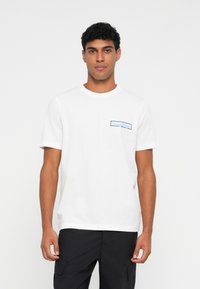 Hvit bomull t-skjorte med korte ermer, rund hals, og et blått "Tommy Hilfiger" logo-patch på venstre bryst.