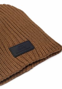 Brązowa dziana czapka z prążkowanym wzorem, z czarną prostokątną metką naszytą z boku.