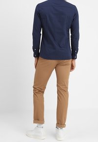 Marineblauwe lange mouwen shirt, van katoenmix, met knoopmanchetten, gecombineerd met beige chino's, van katoen, slim fit, opgerolde manchetten, en witte sneakers.