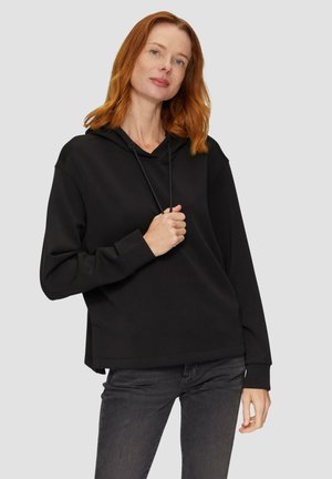 Sweatshirt à capuche noir avec une coupe décontractée, doté d'une poche avant, d'un cordon de serrage et de poignets à côtes, associé à un jean gris foncé.
