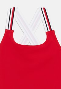 Κόκκινο τοπ μαγιό με λεία υφή, με λευκές τιράντες που φέρουν κόκκινες και μαύρες ρίγες που σταυρώνονται στην πλάτη.