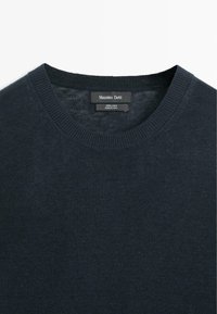 Donkerblauwe trui met ronde hals, geribbelde kraag en het label "Massimo Dutti" dat 100% linnen aangeeft, gemaakt in China.