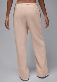 Beige sweatpants met wijde pijpen, elastische tailleband, zijzakken en een gladde textuur, van achteren getoond tegen een neutrale achtergrond.