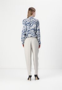 Long-sleeve shirt with blue and white wave-pattern on a light background, paired with light grey trousers and black high-heeled shoes.