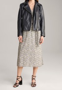 Czarna skórzana kurtka motocyklowa z srebrnymi akcentami nałożona na kwiecistą midi sukienkę w delikatnych kolorach, zestawiona z czarnymi sandałami na słupku z paskami.