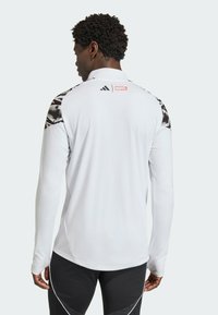 White athletic long-sleeved shirt with black patterned shoulder accents and a red logo, featuring a high collar and fitted design.