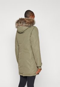 Olivegroene parka met een nepbont capuchon, lange mouwen en zijzakken. De stof lijkt glad met stiksels en heeft een iets getailleerde vorm.
