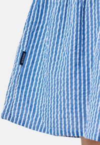 Blue and white striped fabric with textured ripples, featuring a small black label that reads "SEASIDE" at the hem.