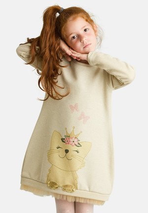 Beige Kleid mit goldenen Farbakzenten, das eine Katzen-Grafik mit einer Krone und Blumen zeigt; Saum verziert mit Tüll. Lange Ärmel und lockere Passform.