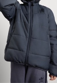 Námořnická prošívaná bunda s obousměrným zipem a kapucí. Obsahuje prošívané panely, elastické manžety a logo Adidas na levé hrudi.