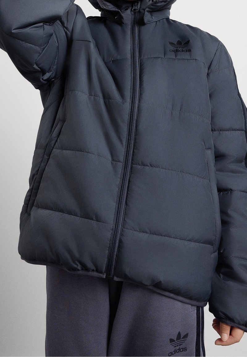 Námořnická prošívaná bunda s obousměrným zipem a kapucí. Obsahuje prošívané panely, elastické manžety a logo Adidas na levé hrudi.