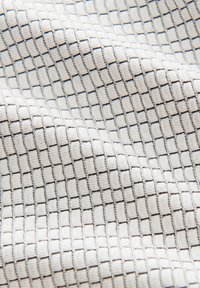 Tissu textile avec un motif en grille texturé en blanc et gris clair, présentant des formes carrées en relief et une texture douce et tissée.
