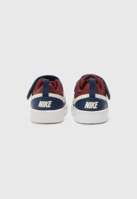 Tênis Nike com uma combinação de cores bordô e azul-marinho, com uma sola branca, fecho de Velcro e um grande logótipo branco na parte de trás.