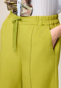 Pantaloni larghi verde lime con vita regolabile, tasche laterali e una texture morbida, caratterizzati da dettagli di cucitura lungo le cuciture.