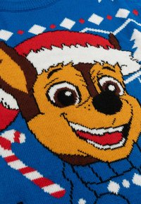 Maglione lavorato a maglia con il volto di un cane dei cartoni animati, su uno sfondo blu, con accenti rossi e fiocchi di neve bianchi. Include dettagli a forma di bastoncino di zucchero.