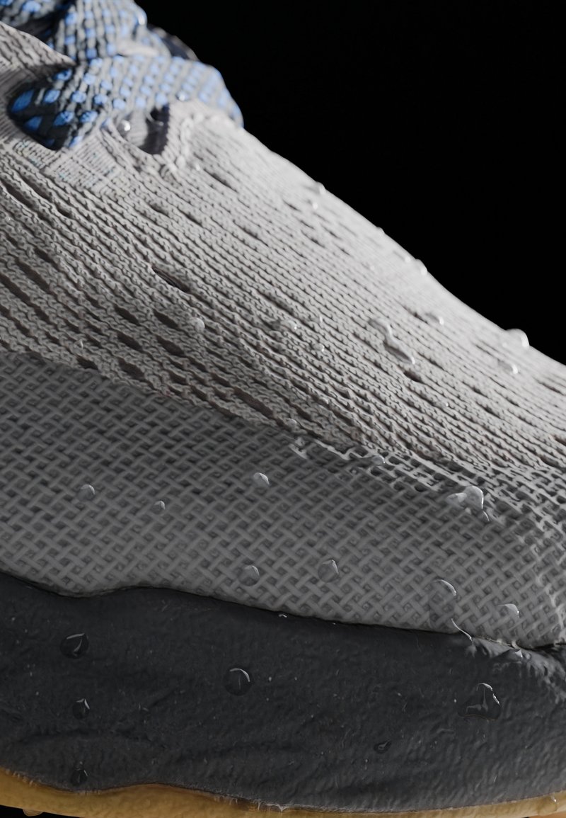 Zapatilla gris con parte superior de punto texturizado, gotas de agua en la superficie, suela de goma negra y cordones azules entrelazados en las ojales.
