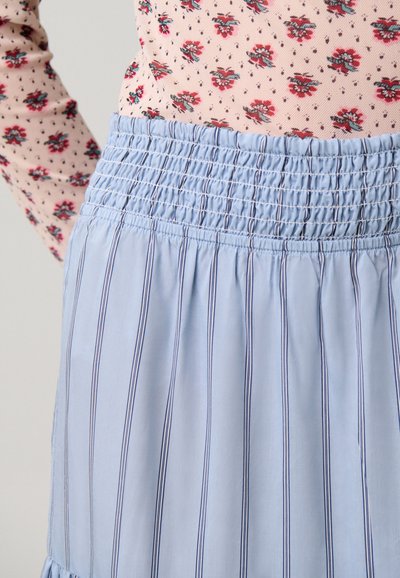 Persona che indossa una maglietta a maniche lunghe floreale rosa chiaro infilata in una gonna a vita alta azzurro chiaro con sottili righe verticali.