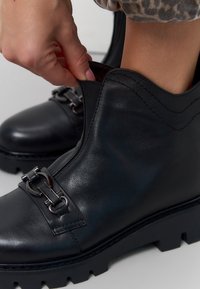 Zwarte leren enkellaarsjes met een chunky zool, voorzien van decoratieve hardware en elastische zij-inserts voor eenvoudig aan- en uittrekken. Textuurafwerking.