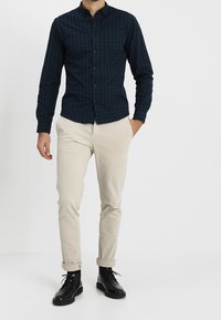 Mörkgrön rutad skjorta med knappar, slim fit, kombinerad med beige chinos och svarta snörstövlar, som framhäver en enkel, modern design.