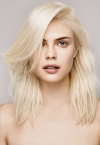 Primer plano de una persona con cabello largo, lacio y rubio platino, piel clara, maquillaje neutro y ojos avellana, contra un fondo suave y neutro.