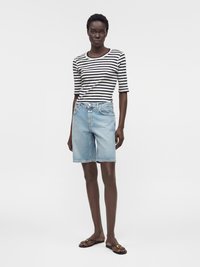 Femme portant un haut à manches courtes rayé noir et blanc, un short en jean bleu clair longueur genou et des sandales plates noires.