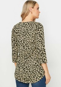 Leopardmönstrad tunika med trekvartslånga ärmar, tillverkad av mjukt tyg i beige och svart; har en rundad avslutning och sidfickor.