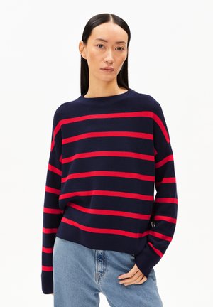 Marineblauwe trui met gedurfde rode horizontale strepen, ronde halslijn en relaxte pasvorm. Getextureerde brei en afhangende schouders. Gepaard met lichtblauwe jeans.