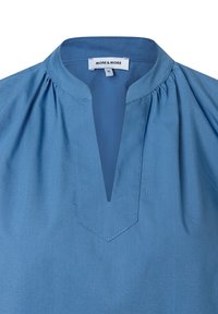 Blaue Bluse mit Stehkragen, gefertigt mit Falten an den Schultern und einem V-förmigen Ausschnitt. Hergestellt aus glattem Stoff mit sauberer Nahtführung.
