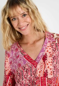 Blouse multicolore avec un design en V, ornée de motifs floraux et paisley complexes dans des nuances de rose et de rouge, en tissu doux et léger.