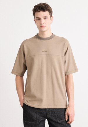 Short-sleeve, beige t-shirt featuring a crew neckline and subtle logo detail in a contrasting shade. Made of soft, smooth fabric.