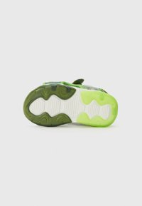 Semelle extérieure de basket verte et noire avec des motifs ondulés, dotée d'un accent vert translucide au niveau du talon et d'une semelle intermédiaire texturée blanche.