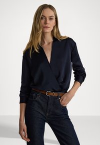 Navy wikk blouse van zachte stof met lange mouwen, gecombineerd met donkere denim jeans en een bruine leren riem met een zilveren gespsluiting.