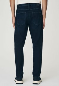 Jeans din denim de culoare albastru închis, cu o croială dreaptă, două buzunare la spate și o ajustare la glezne. Prezintă un eticheta pe talie.
