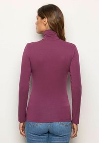 Langärmliges Rollkragenoberteil, lila, figurbetontes Design, glatte Textur. Getragen mit hoch taillierten blauen Jeans, Ansicht von hinten.