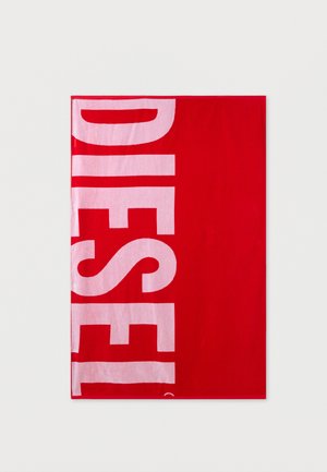 Tissu rectangulaire rouge avec un texte vertical grand, audacieux et rose clair indiquant "DIESEL", plié sur un fond blanc.