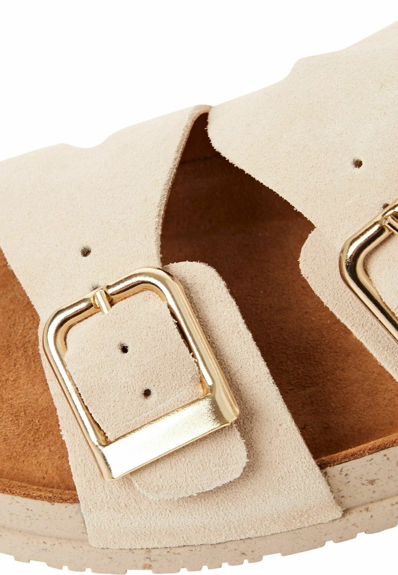 Beige suède sandaal met twee brede banden, gouden metalen gespen en een textuurvoetbed met een lichtgekleurde zool.