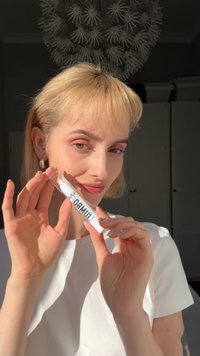 Hvid hudplejetube mærket "JUMBO" holdt af en person. Tuben har en klar hætte og et elegant design. Personen bærer en hvid T-shirt og har lyst hår.