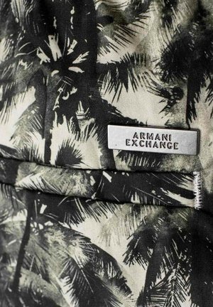 Svart och vit mönstrad tyg med palmblad, med en silverfärgad rektangulär tagg graverad med "ARMANI EXCHANGE."