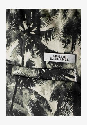 Mustavalkoinen kuvioitu kangas, jossa on palmulehtiä, ja hopeinen suorakulmainen tunnus, jossa lukee "ARMANI EXCHANGE."