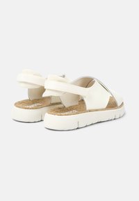 White sandals with an open design, featuring elastic straps and a cork insole. The sole is thick and textured for grip.