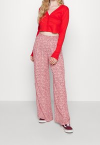 Red ribbed long-sleeve crop top with buttons paired with wide-leg pants featuring a small floral pattern in shades of pink and red.