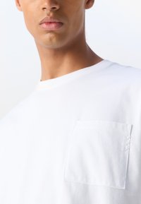 Vit bomull T-shirt med rundad halsringning och en kvadratisk bröstficka med dekorativ sömnad på ena sidan. Slät textur, klassisk design.