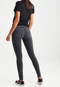 Jeans ajustados de talle alto en negro con una textura suave y bolsillos traseros. Combinados con una camiseta negra y zapatillas negras.