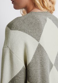 Strickpullover mit einem hellgrünen und grauen Diamantmuster, ausgestattet mit einem gerippten Ausschnitt und weicher Textur. Sichtbare Nahtdetails an der Schulter.